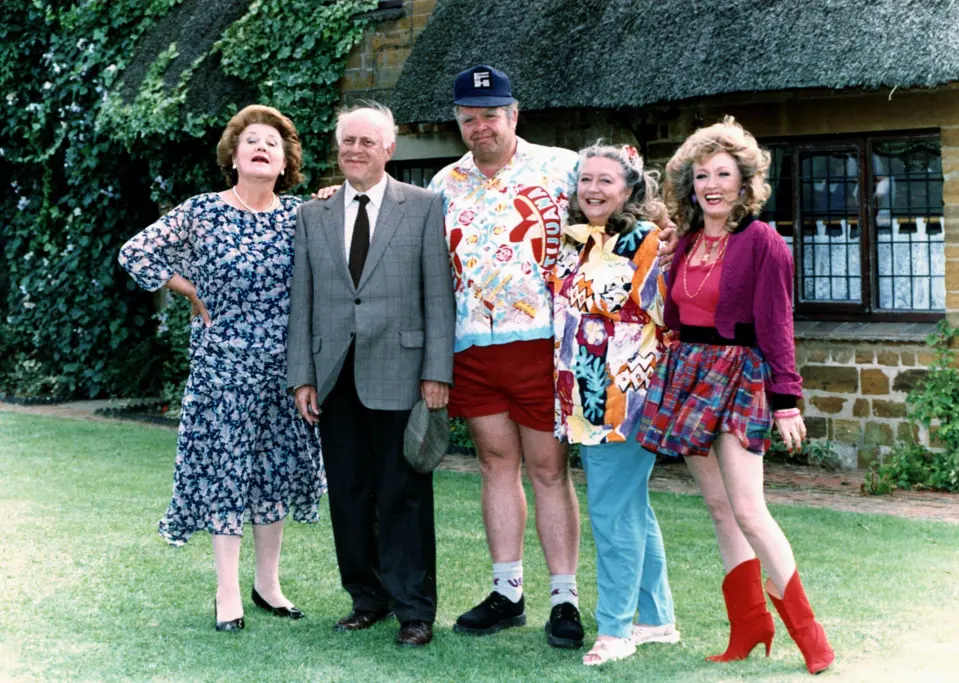 The cast of Keeping Up Appearances poses on a lawn, including Patricia Routledge, Clive Swift, Geoffry Hughes, Judy Cornwell & Mary Miller.