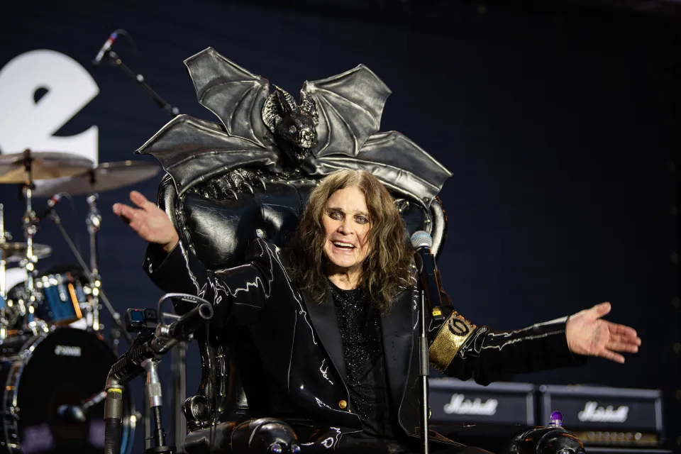 Ozzy Osbourne sitting in a black leather throne with a bat-like headrest, speaking into a microphone.