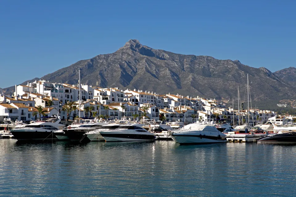 Puerto Banus with luxury yachts, white buildings, and a mountain in the background.