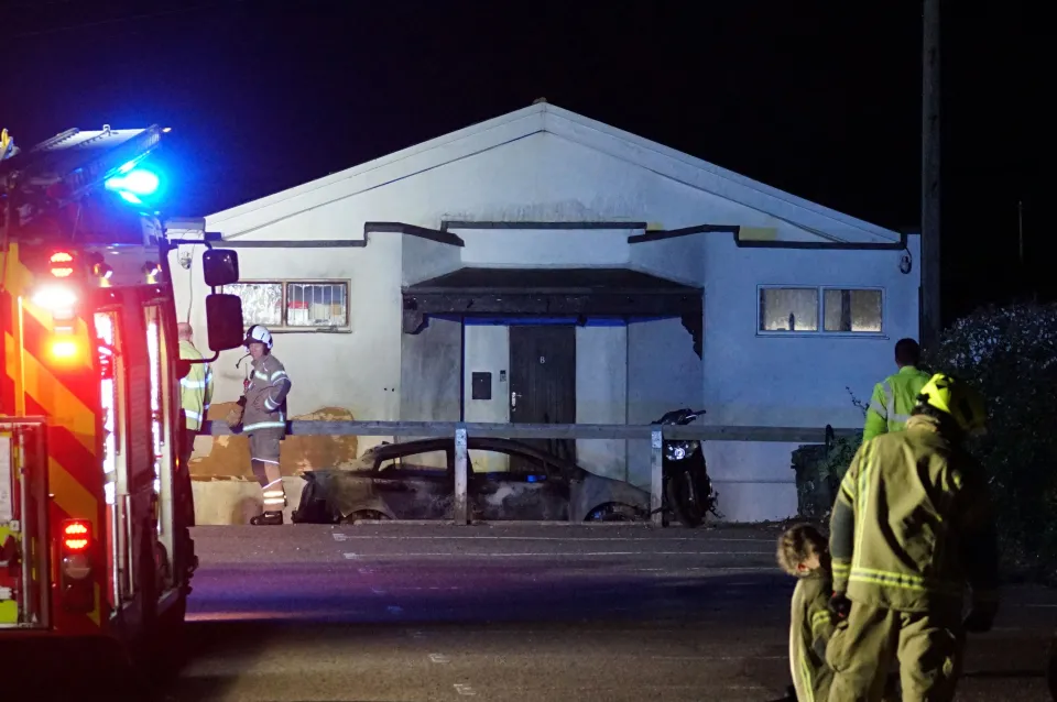 The Peachaven Mosque with a burnt-out car in front, fire engine lights visible, and firefighters on scene after an arson attack.