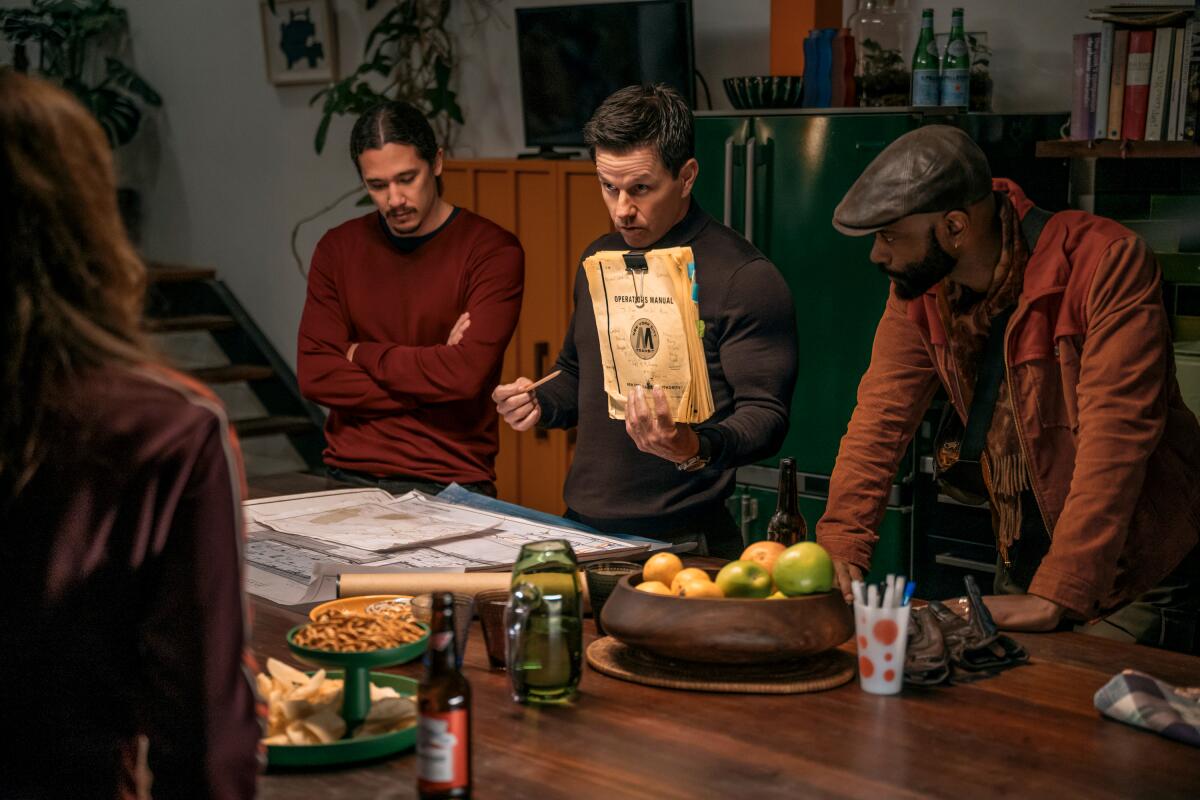 Three men stand behind a table and one holds up a stack of papers clipped together.