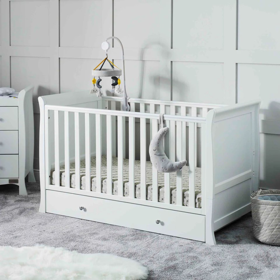 White wooden cot bed with a mobile and a hanging moon toy.