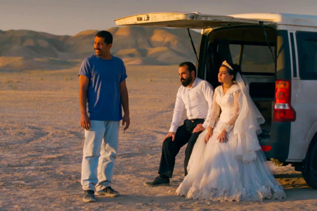 Several people wait in the desert by a truck.