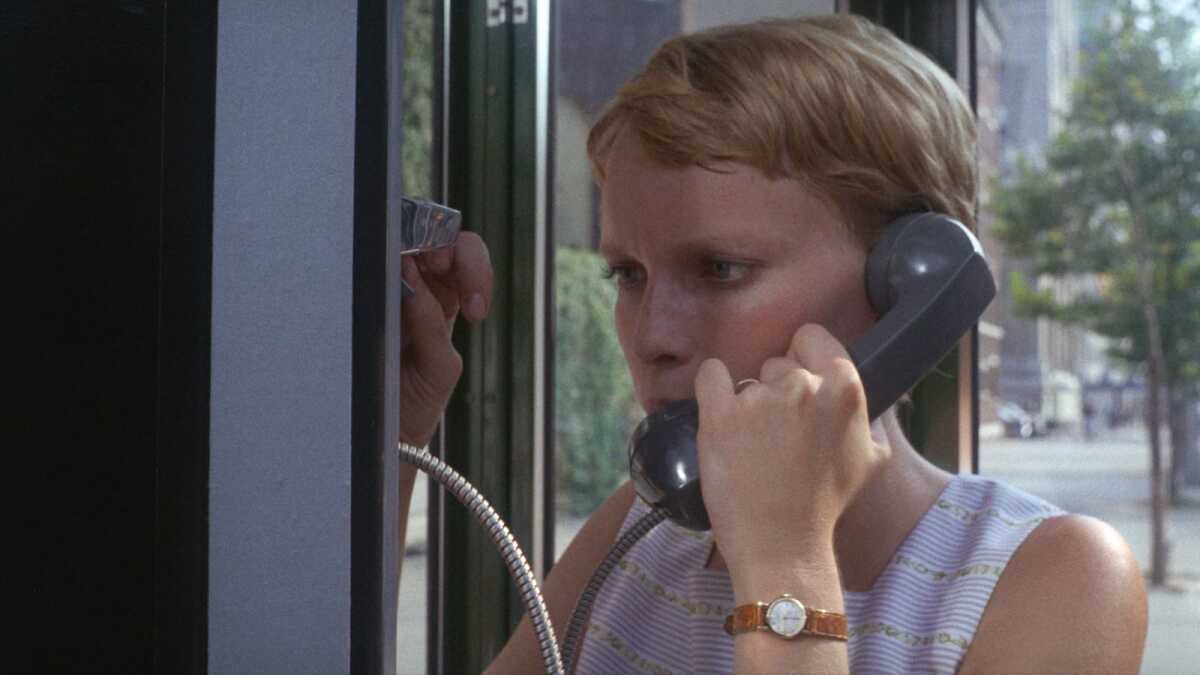 A woman speaks urgently into a pay phone.