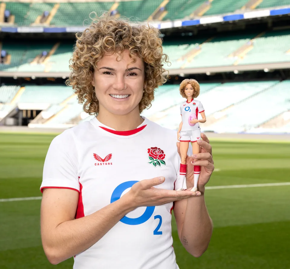 Ellie Kildunne, an Olympic medallist, social media star, and body positivity advocate, holds her custom Barbie doll, both wearing England Rugby 'Red Roses' jerseys.