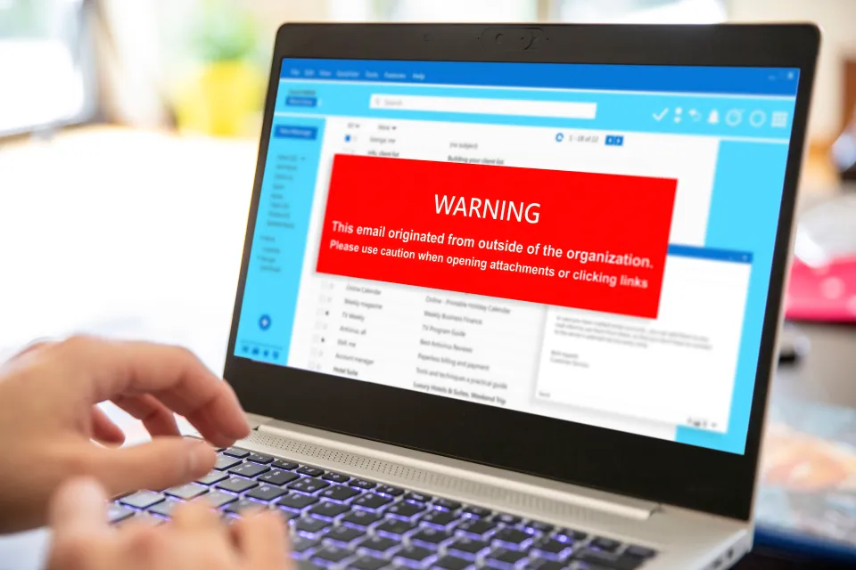 Laptop screen displaying an email with a red warning banner about external origin and attachments.