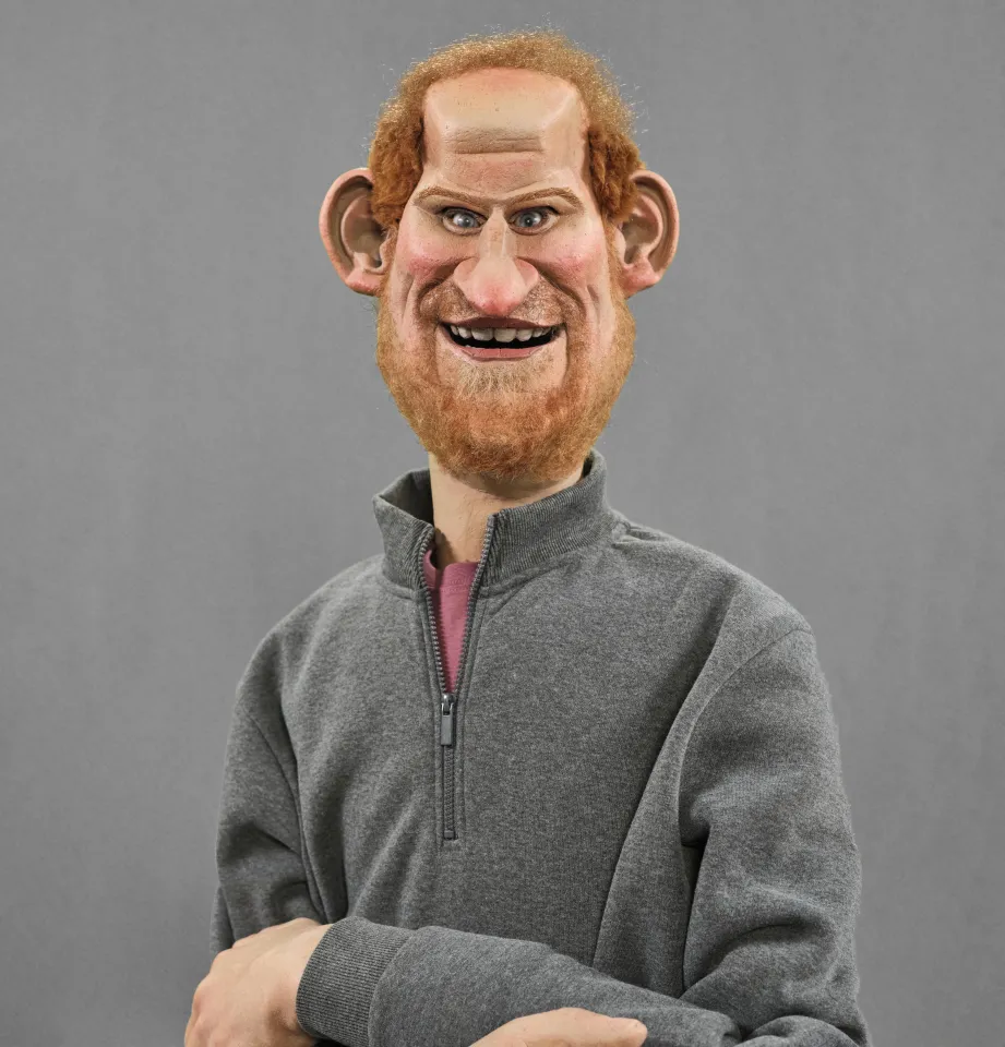 Illustration of a puppet resembling Prince Harry, wearing a grey zip-up top over a pink t-shirt.