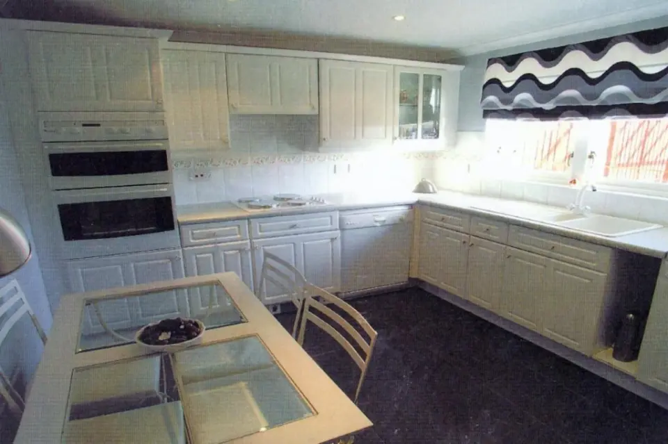 A kitchen with white cabinets, a black counter, and a table with a bowl of dried fruit.