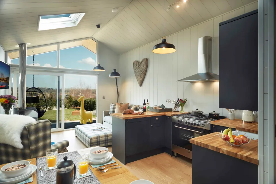 Interior view of a modern open-plan kitchen and living area, featuring dark blue cabinets, wooden countertops, and a dining table set for breakfast.