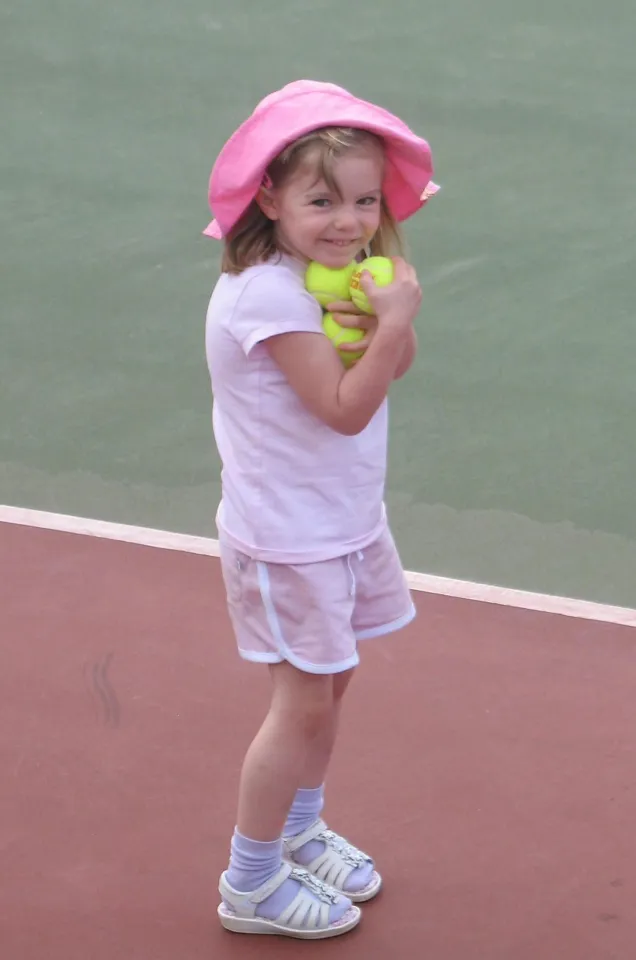 A young girl wearing a pink hat and outfit, holding tennis balls, standing on a tennis court.