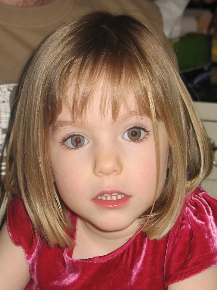 Madeleine McCann with short blonde hair and green-brown eyes, wearing a red top.