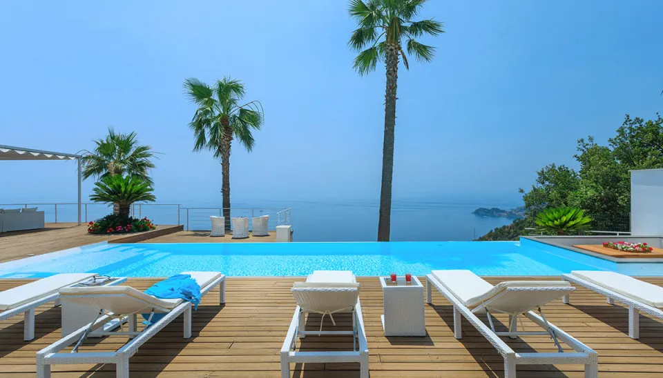 Infinity pool overlooking the sea with lounge chairs and palm trees.