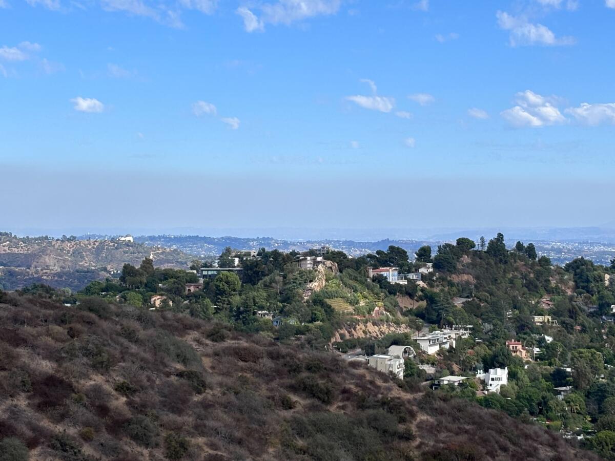 Lush hillsides, some dotted with houses, and a bright blue sky with a layer of gray smog.
