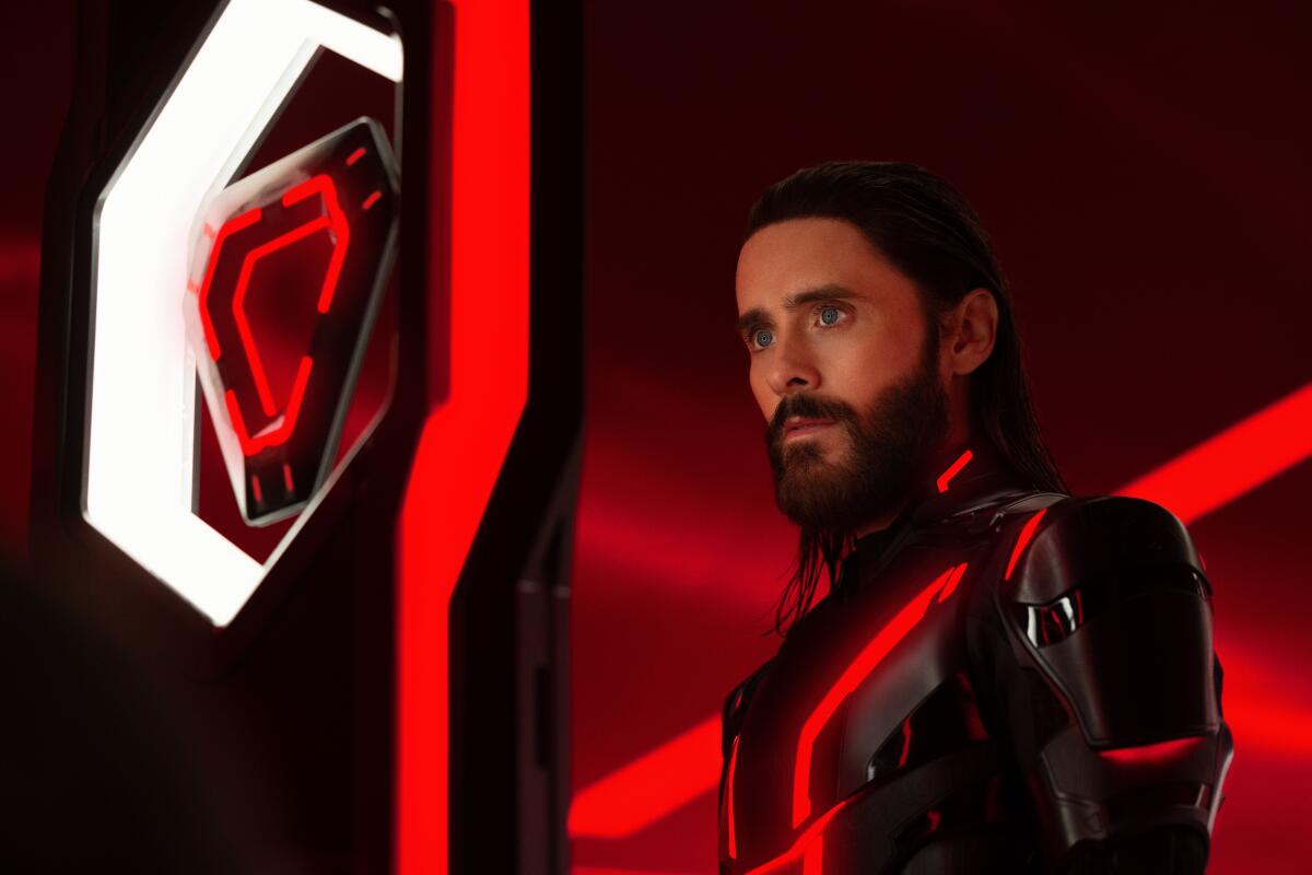 Jared Leto in a futuristic bodysuit looking at a floating triangle