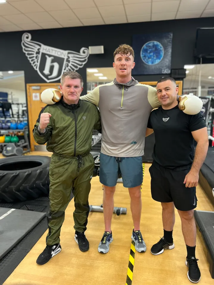 Three men posing in a gym, with boxing gloves on two of them.