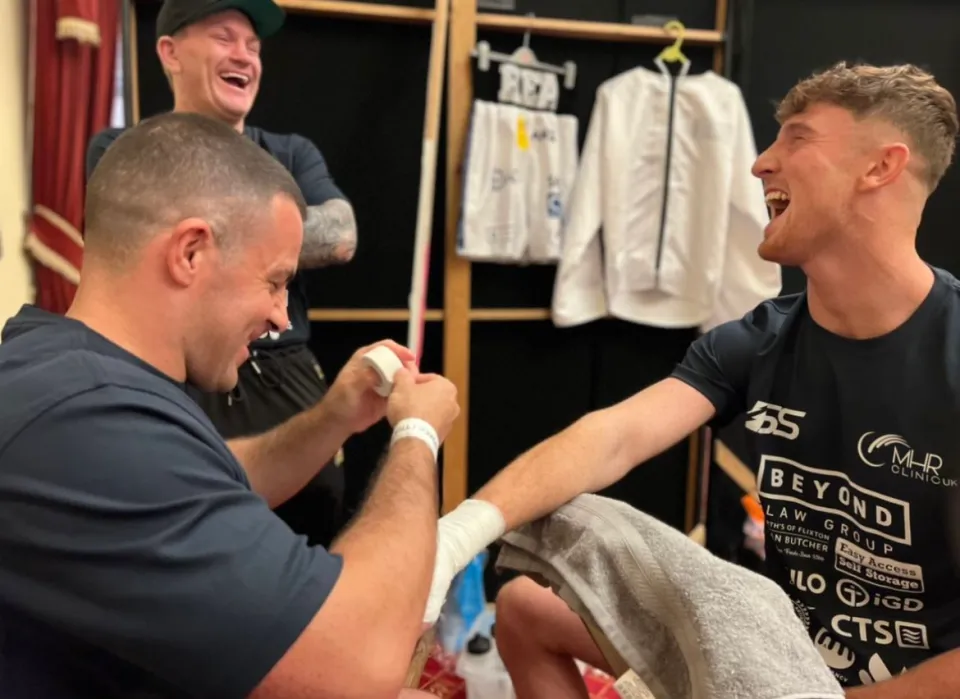 A boxer getting his hands wrapped with two other men laughing in the background.