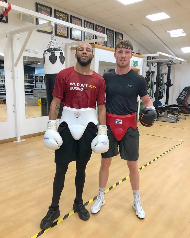 Two boxers in protective gear stand in a gym.