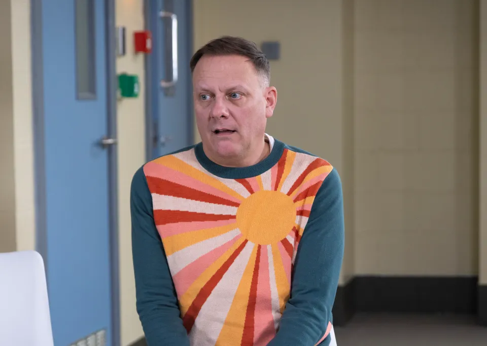 Sean Tully, played by Antony Cotton, wearing a teal sweater with an orange and pink sunburst pattern.