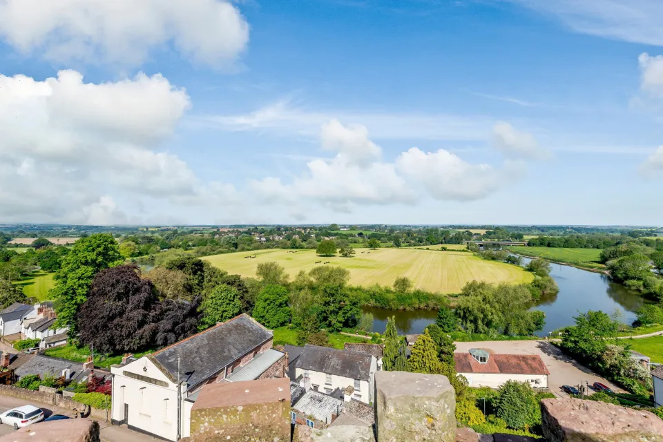 A panoramic view of the Ross-on-Wye countryside, showing buildings in the foreground, fields, a river, and a cloudy sky.
