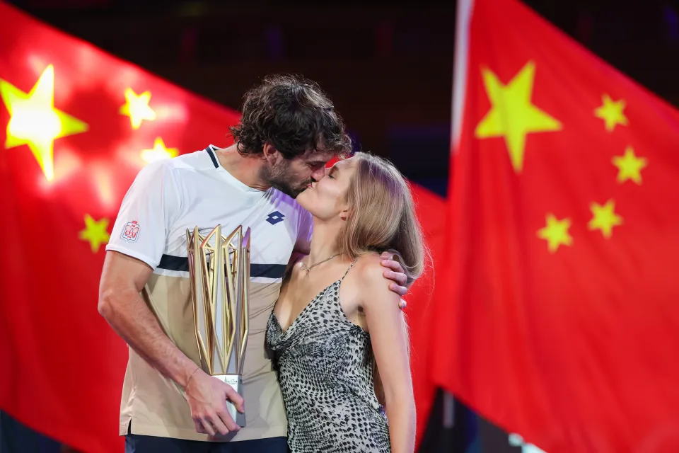 Valentin Vacherot kisses his girlfriend Emily Snyder while holding a trophy during an awards ceremony.