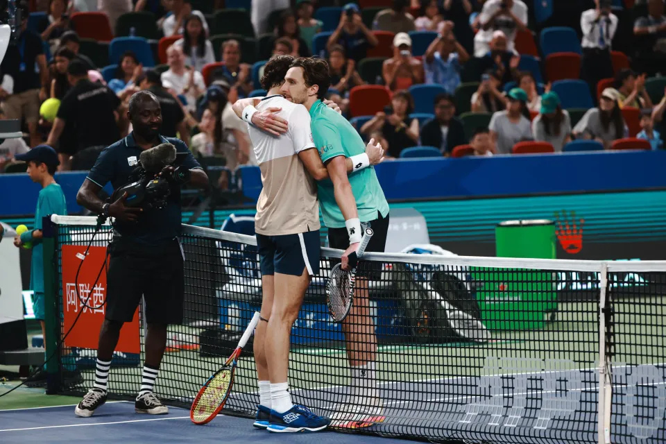 Arthur Rinderknech and Valentin Vacherot hug each other on a tennis court.