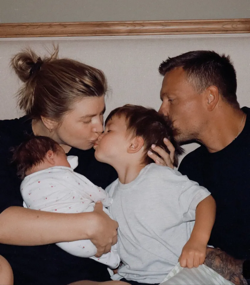 A family of four, including a newborn, a young child, a woman, and a man, all kissing one another.