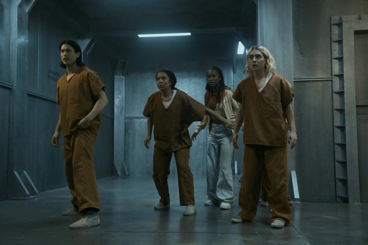 A group of people in prison-like uniforms stand on guard.