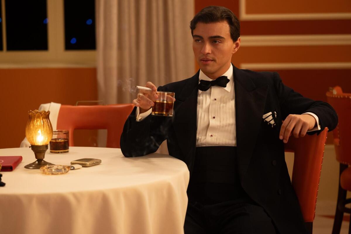 A man in a tuxedo smokes a cigarette at a bar table.