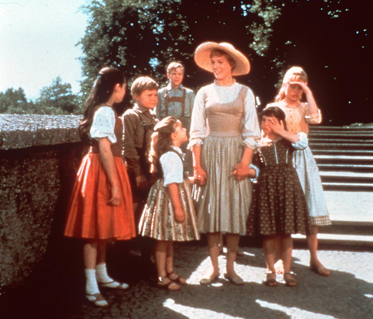 A woman stands among several children in a park.
