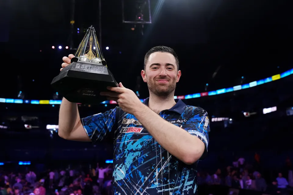 Luke Humphries holding a darts trophy aloft.