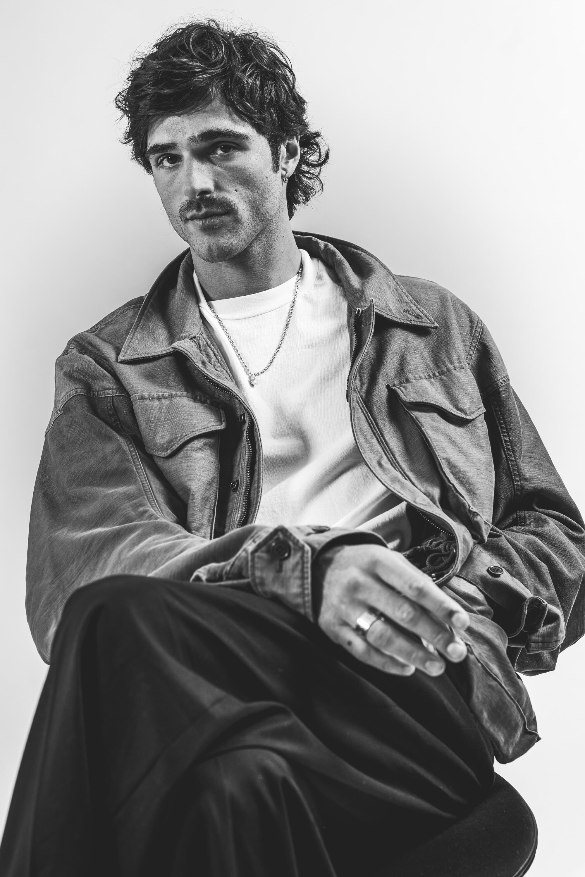 An actor in a white shirt and jacket looks into the lens.