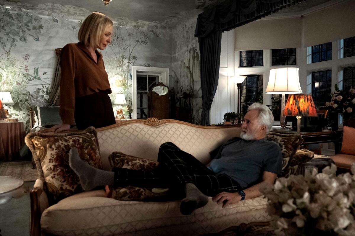 A standing woman looks down at a man lounging on a sofa.