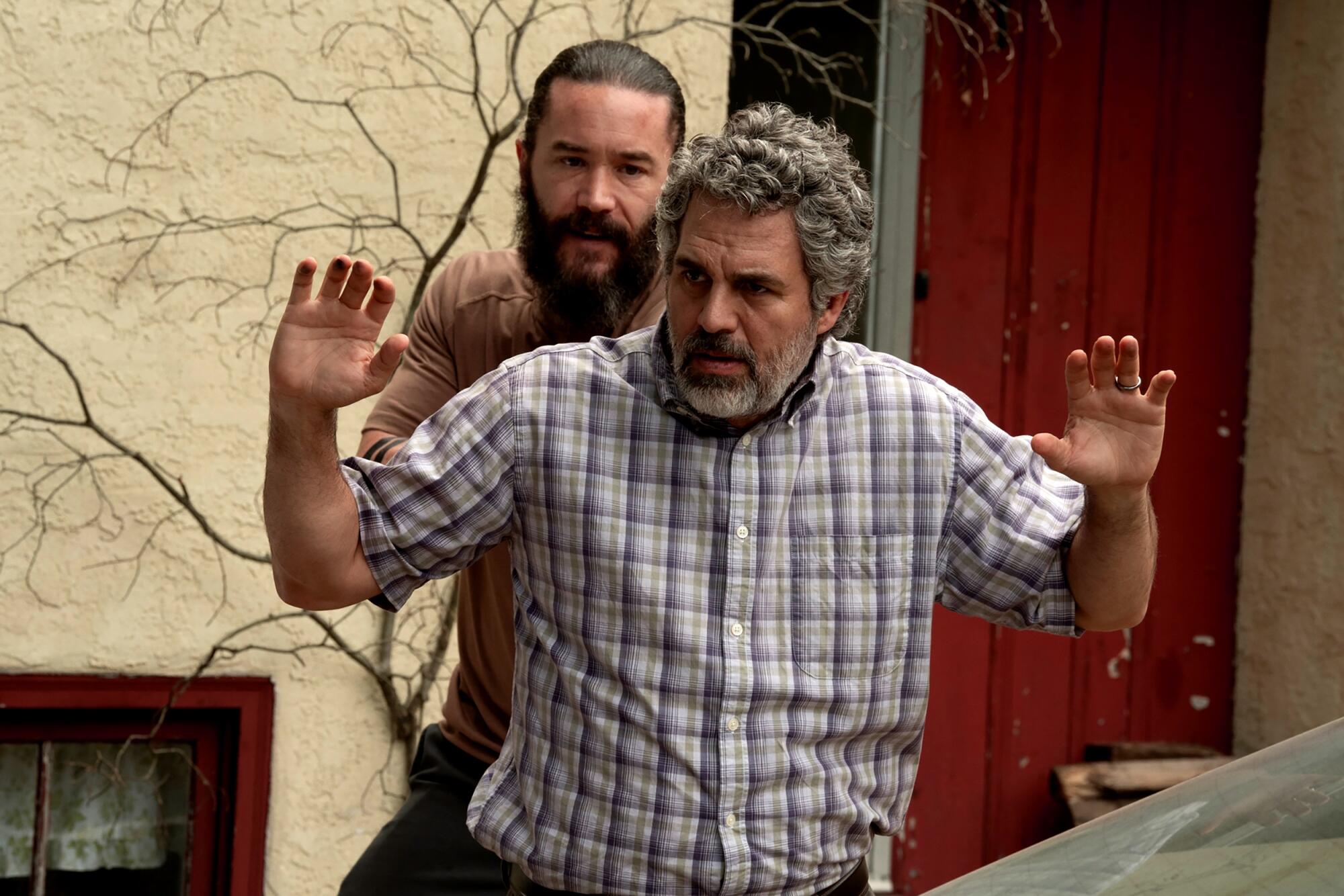 A man stands behind another man who is surrendering with his hands up
