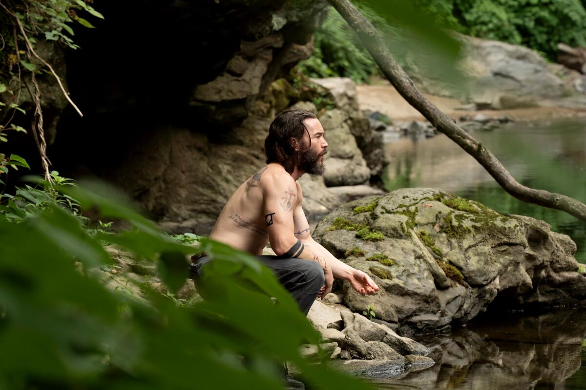 A shirtless man gazes out at a river bank.