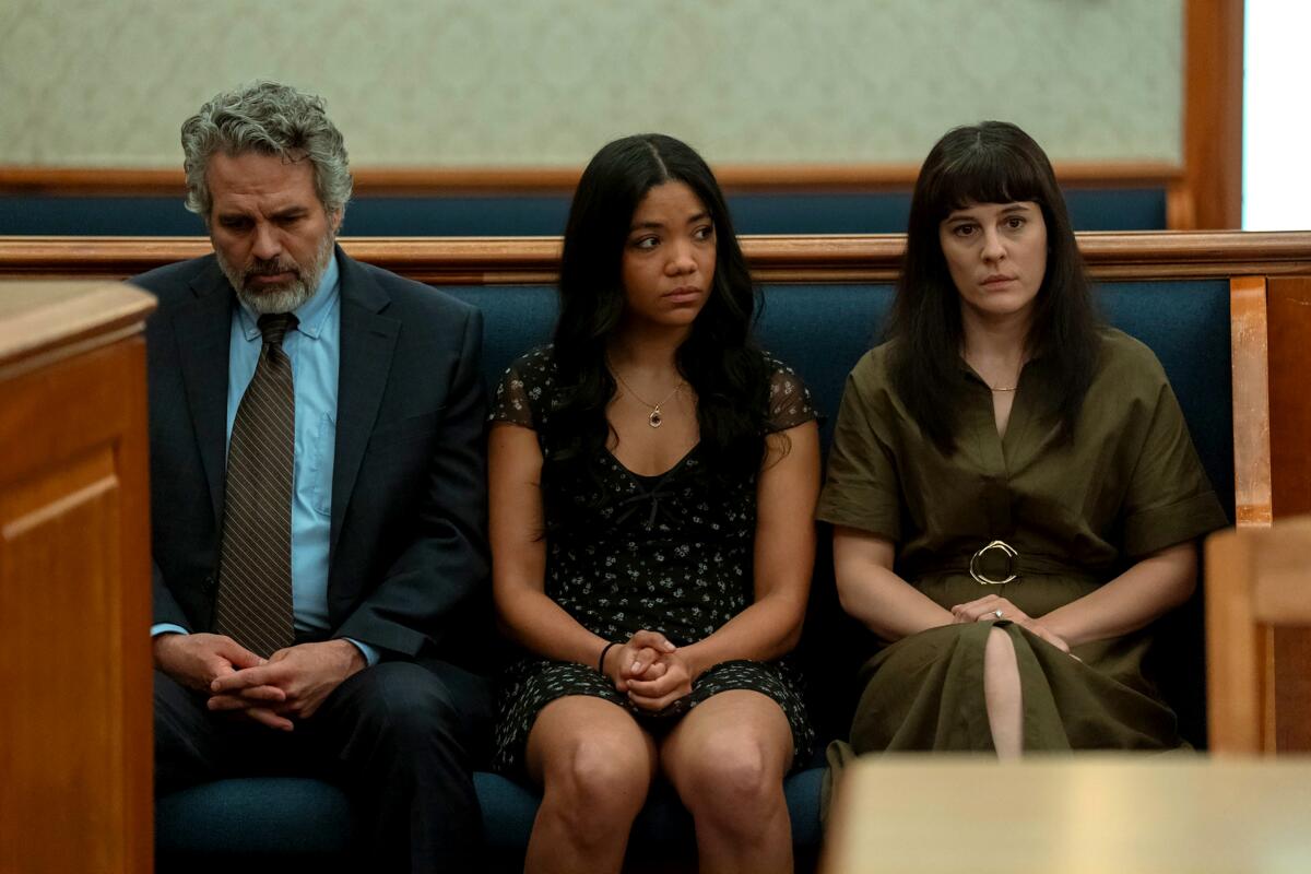 A man in a suit and tie sits alongside two young women