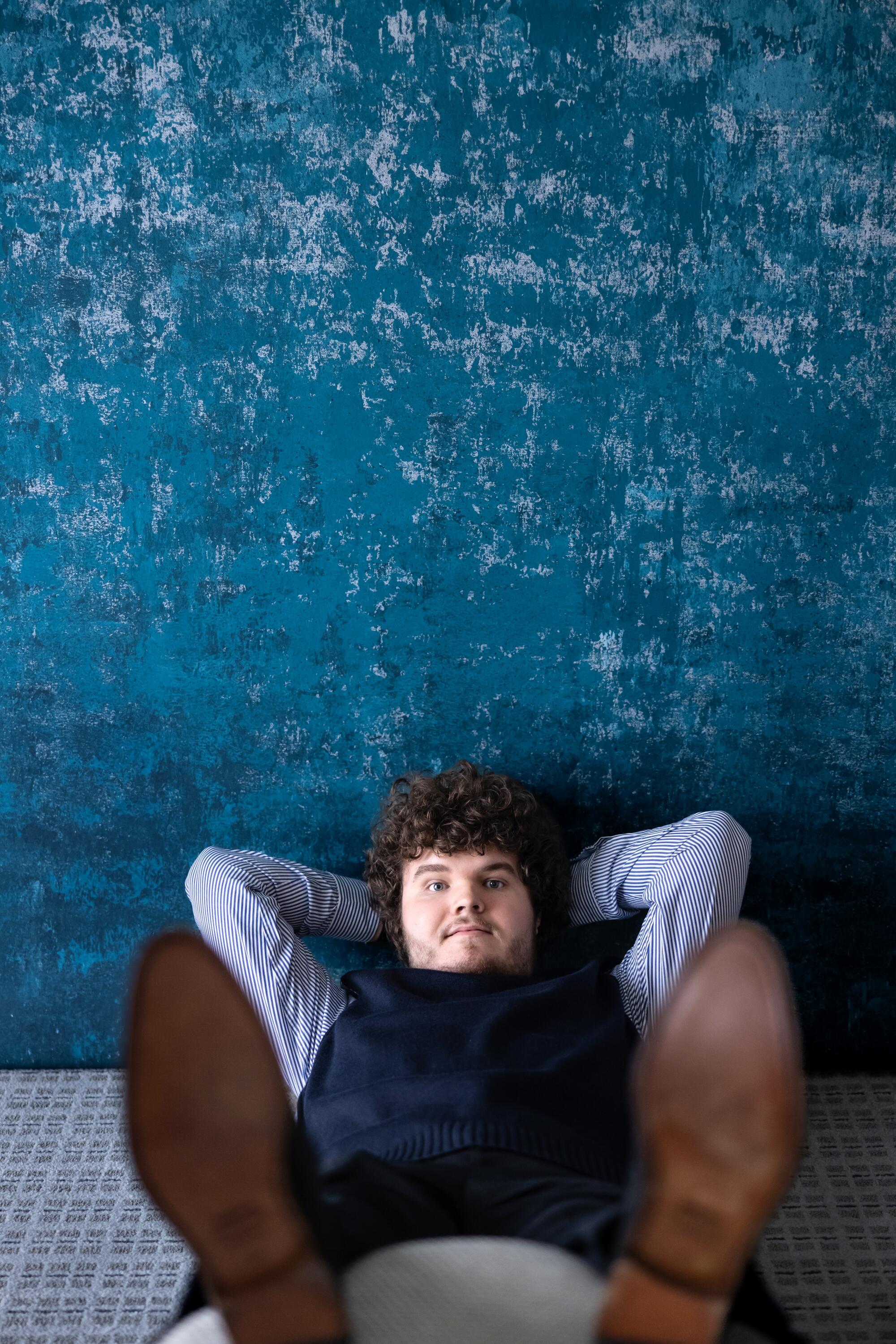A young actor leans back, his arms behind his head.
