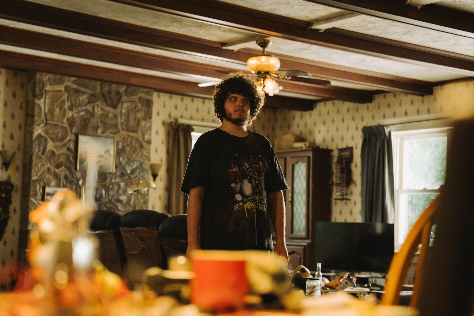 A man in a black t-shirt stands in a kitchen.