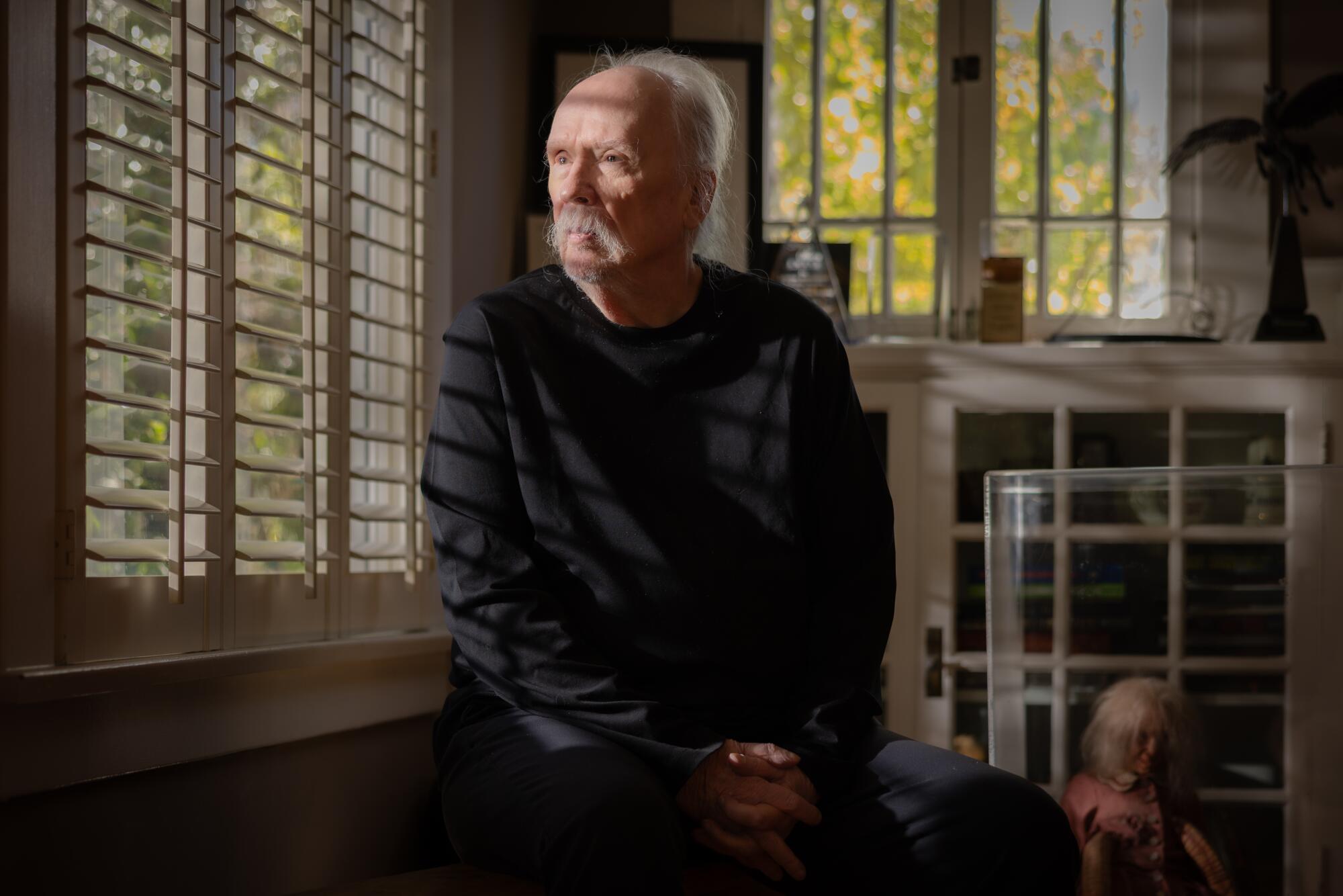 A man sits behind a slatted blind in a living room.