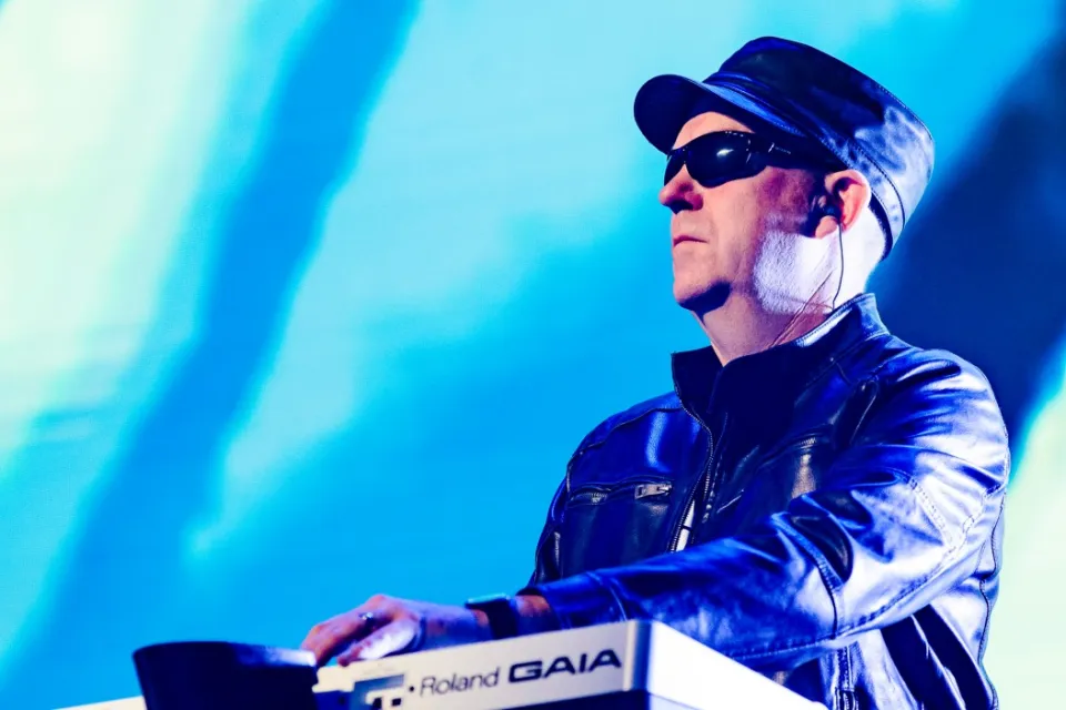 Musician wearing sunglasses, a hat, and a leather jacket playing a Roland GAIA synthesizer.