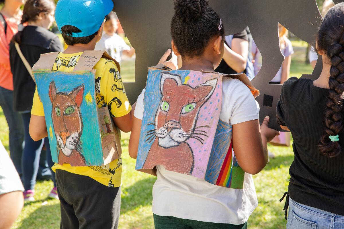 Children wear sandwich boards with colorful paintings of a mountain lion on the back.