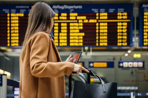 A woman traveller checks her mobile phone in front of the airport's flight information board