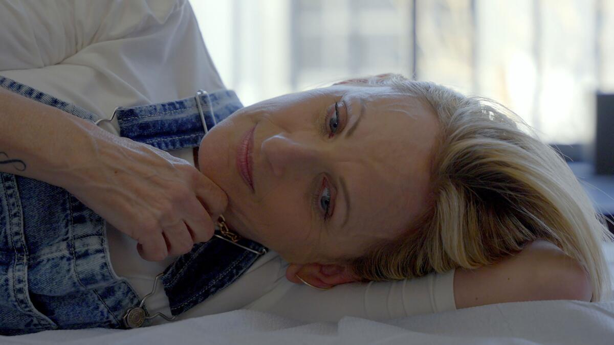 A blonde woman in overalls lies on her side