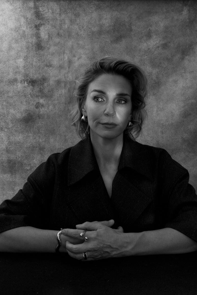 A woman seated in a dark outfit with her arms crossed in front of her.