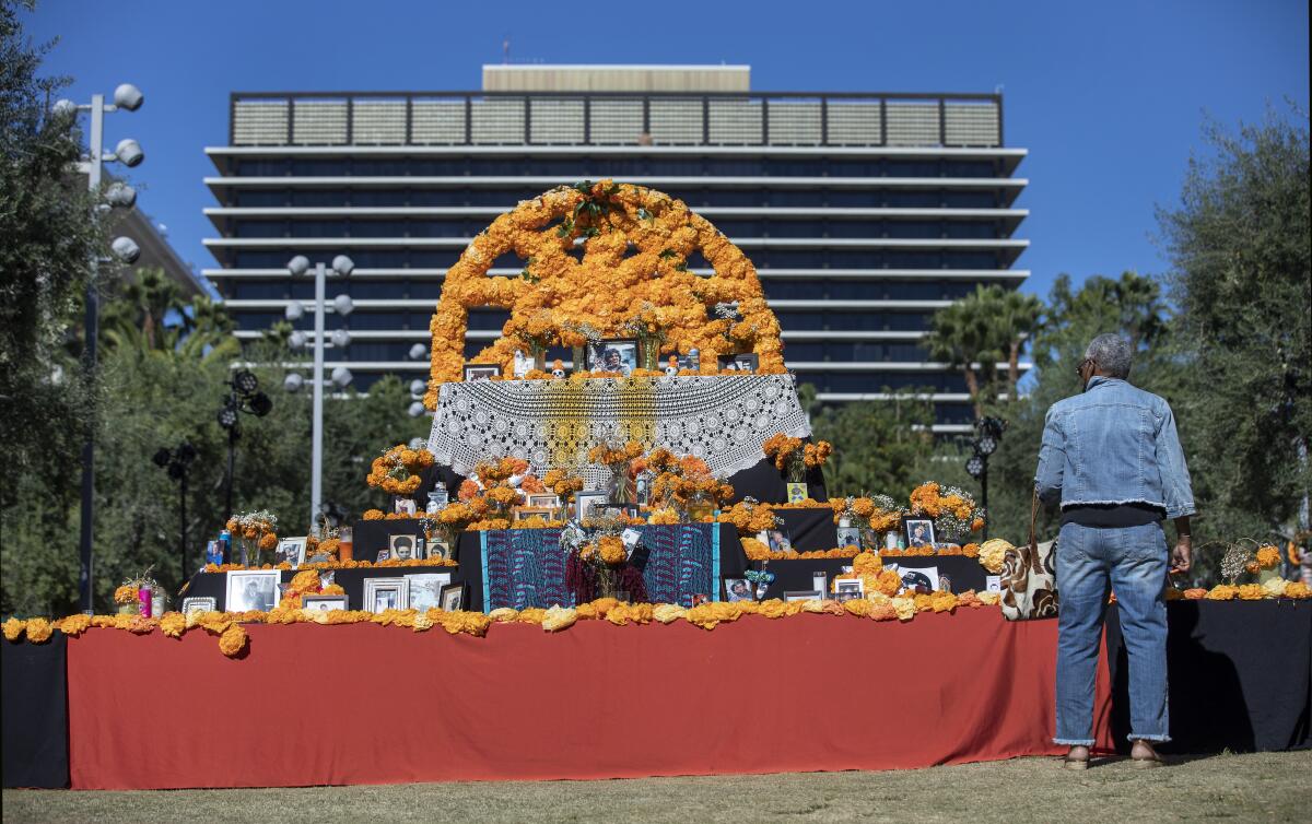 A person stands in front of a large community altar covered in orange marigolds, photographs and candles.