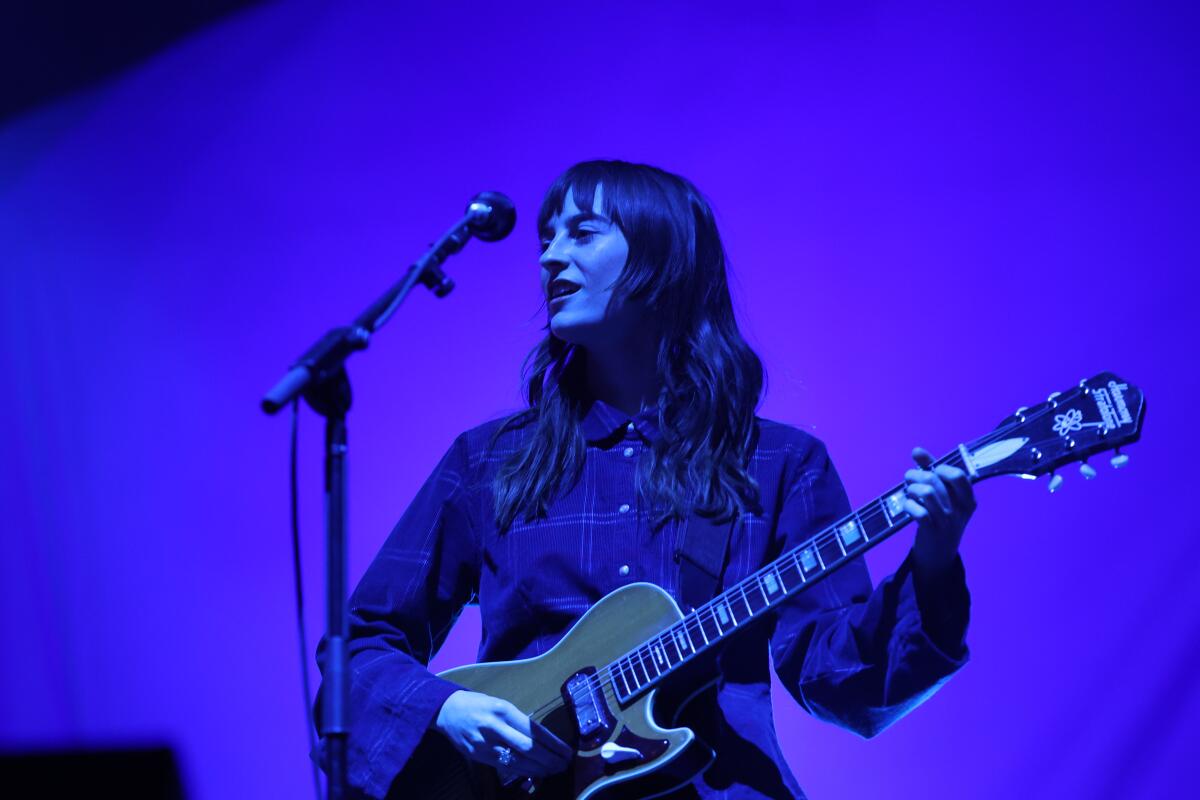 A woman singing and playing guitar onstage.