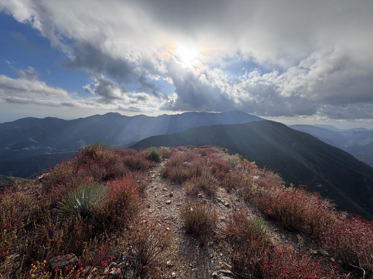 Sunrays shine through white clouds above a mountain range.