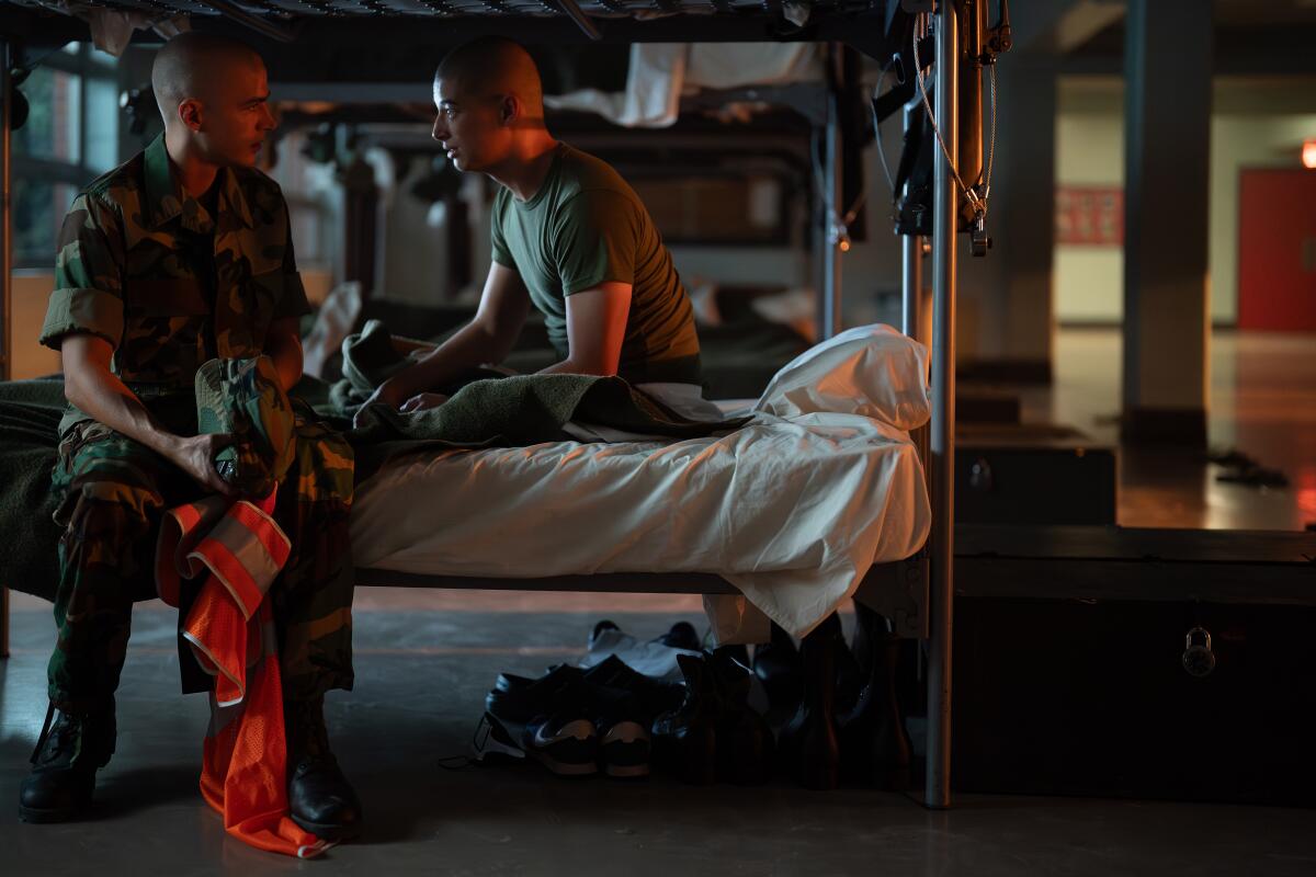 Two men sit on a bottom bunk bed.