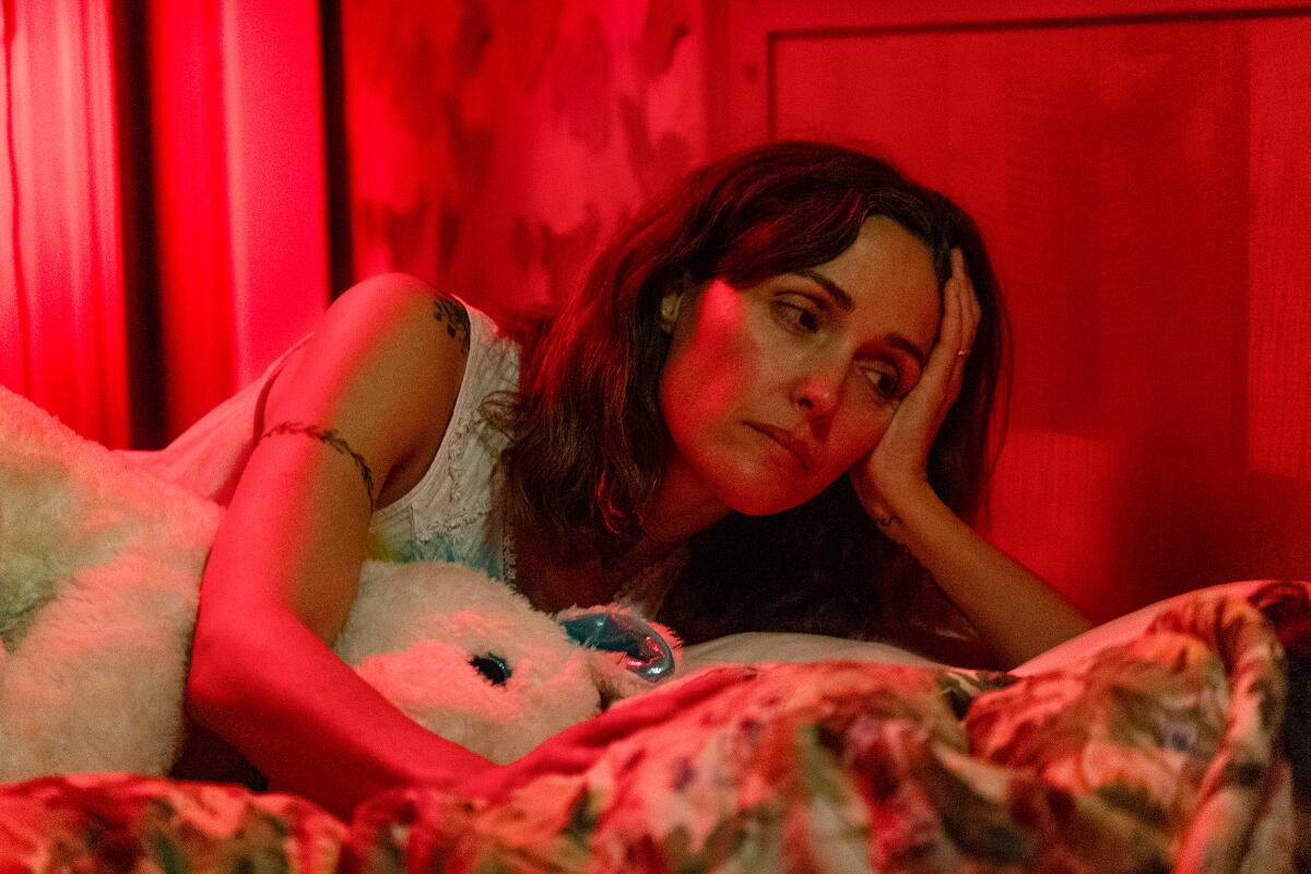 A mother leans on her daughter's bed, concerned.