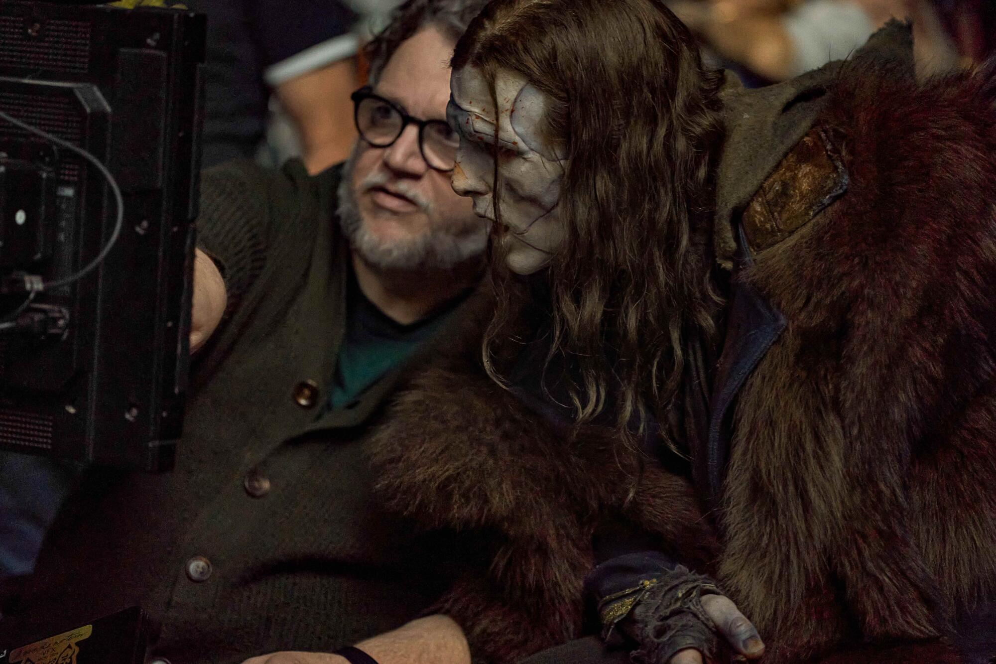 An actor in creature makeup confers with his director behind the camera.
