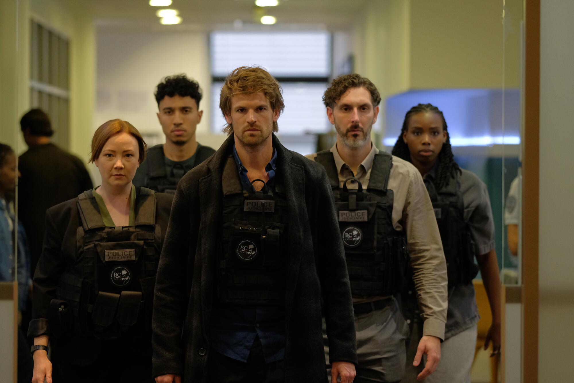 A group of people walking down the hall in Kevlar vests.